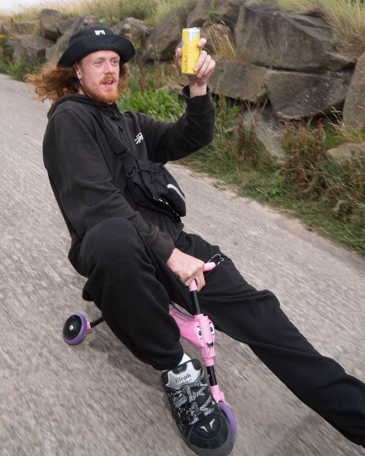 Skater shows off his drink riding downhill on a scooter