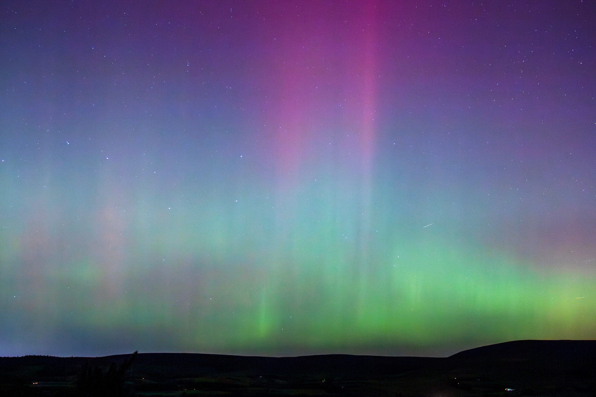 Aurora pillars above a silhouetted ridge of hills