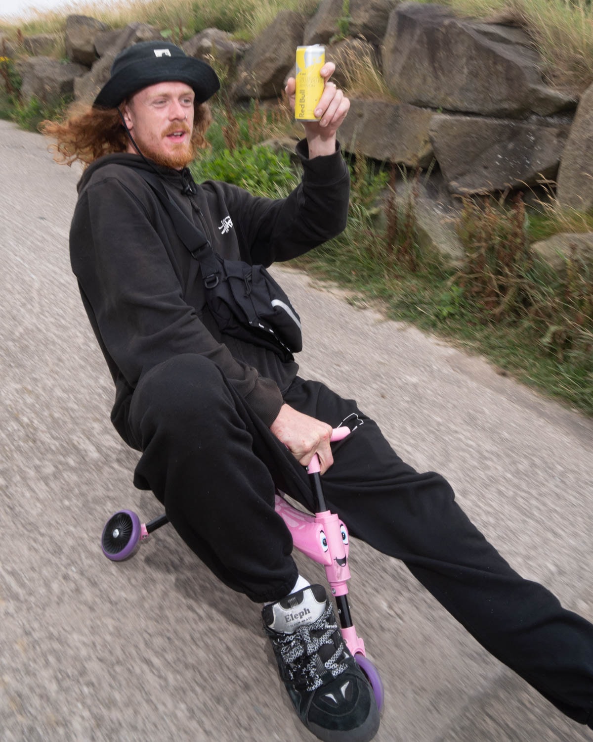 Skater shows off his drink riding downhill on a scooter