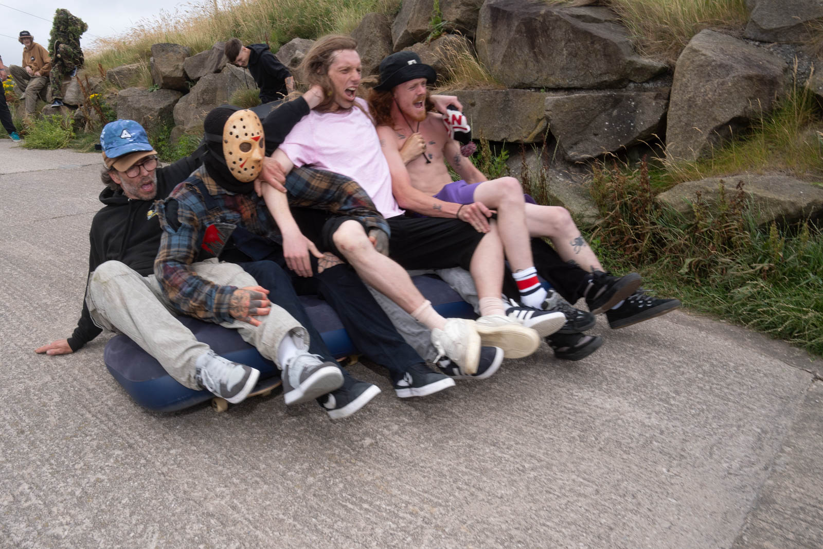 A group rides downhill together, sat across multiple skateboards